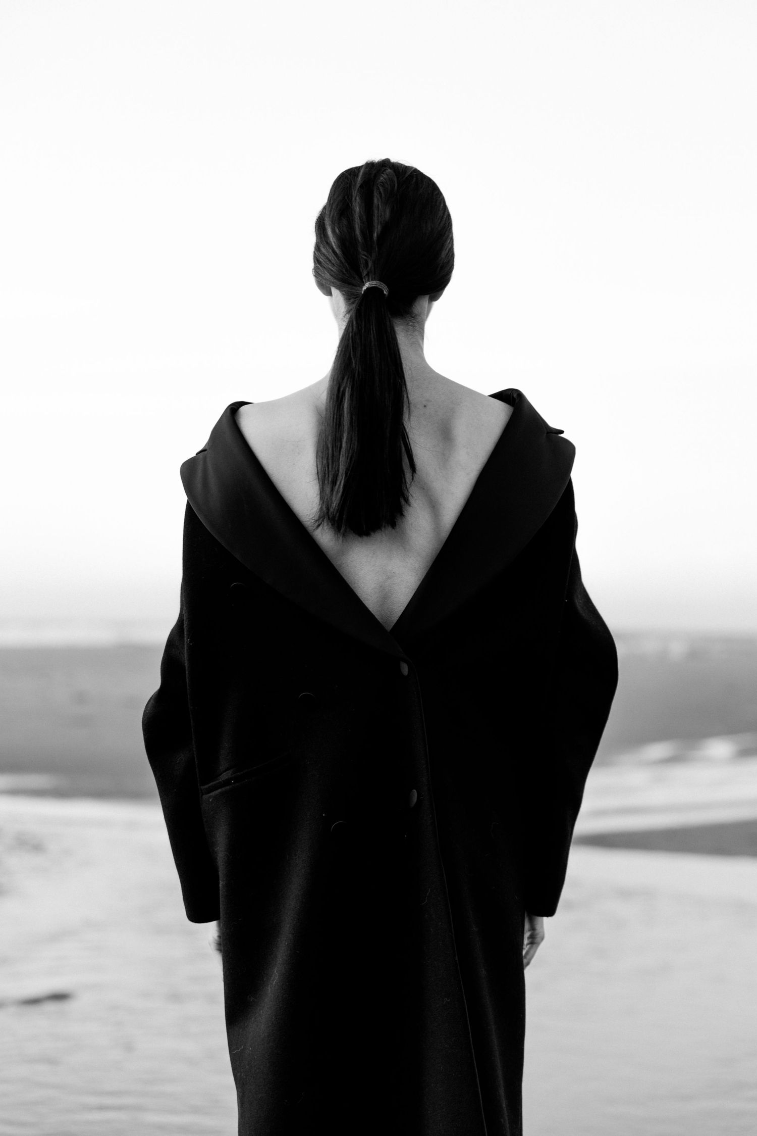 Back view of person in black coat against minimal background.