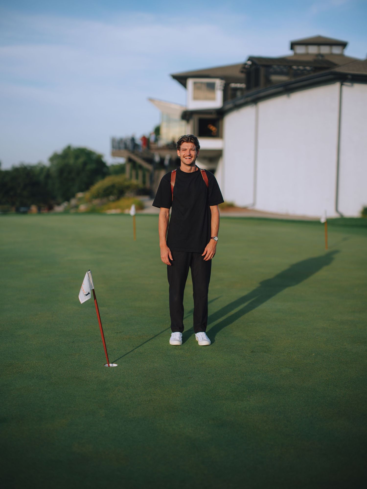 Person standing on a putting green at a golf course with clubhouse in background.