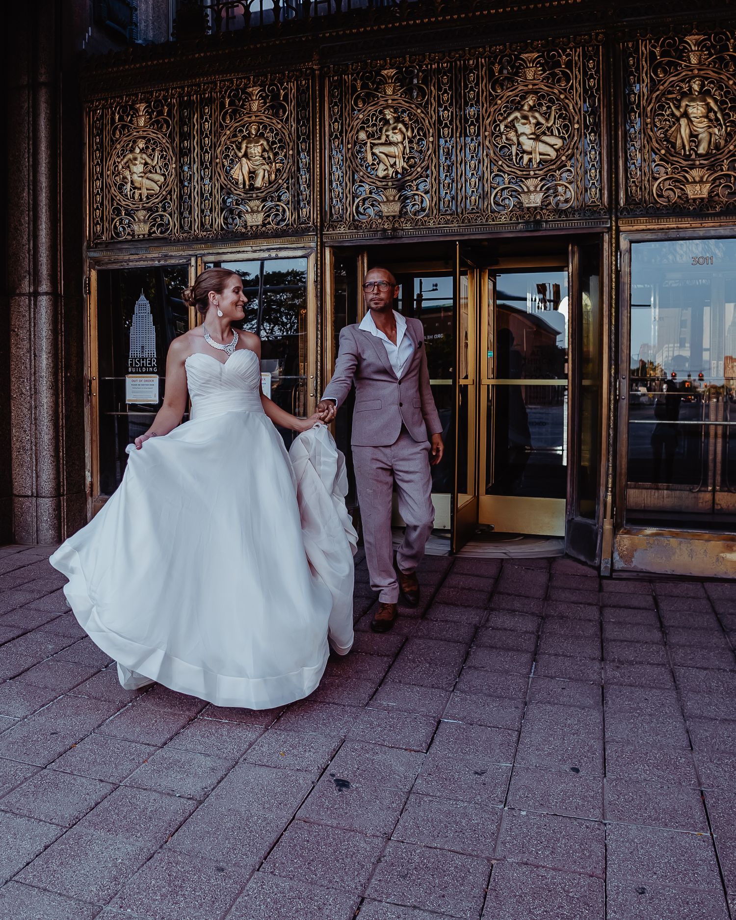 Newlyweds exit ornate building with decorative golden details above entrance.