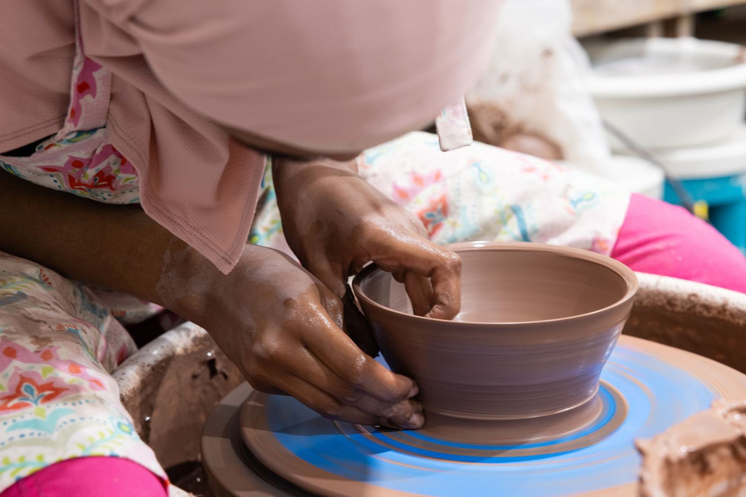 Hands shaping clay on a pottery wheel, forming a smooth brown bowl in a ceramics studio.