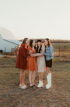 Group wearing coordinated retro outfits huddles together for photo in front of rural barn.