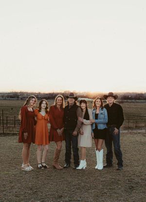 Group in coordinated vintage outfits poses together on farm property at sunset.