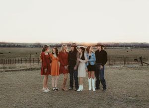 Friends in retro-inspired clothing gather for group photo on rural farmland at dusk.