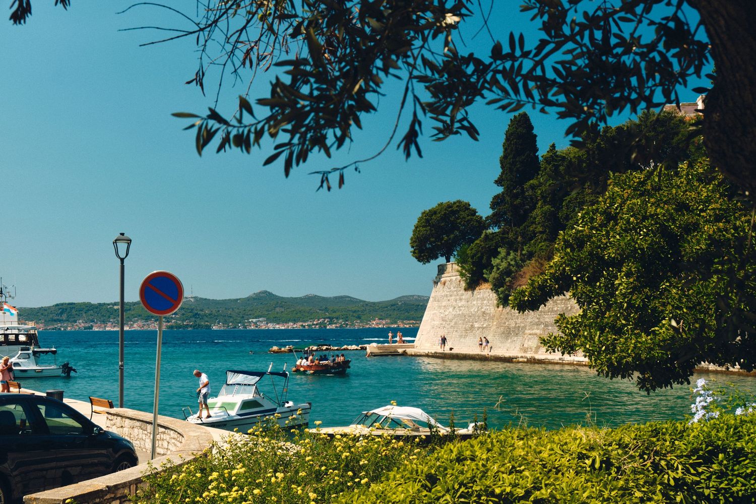Mediterranean coastal scene with boats anchored near historic stone fortification.