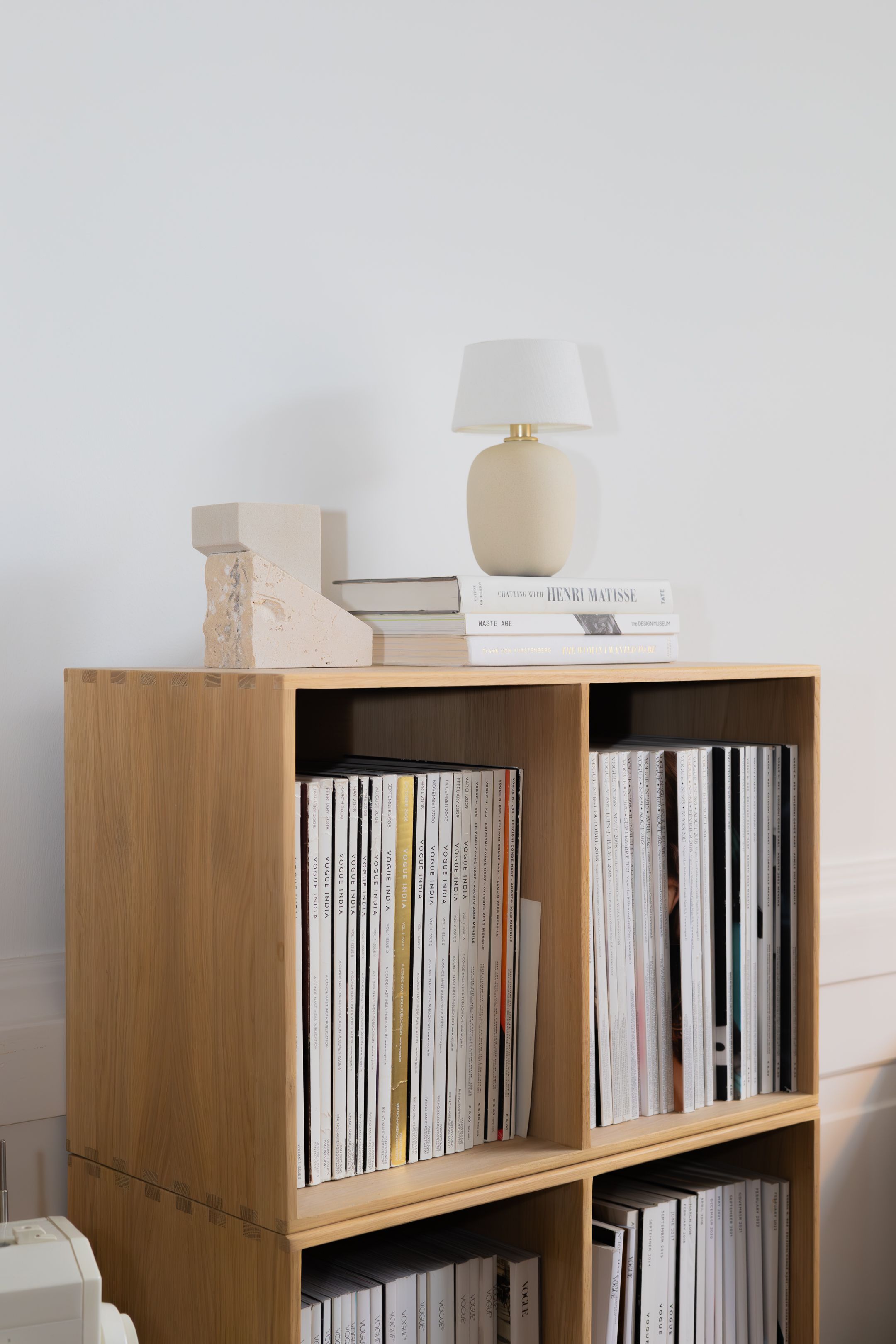 Modern wooden bookshelf storing vinyl records with table lamp on top against white wall.