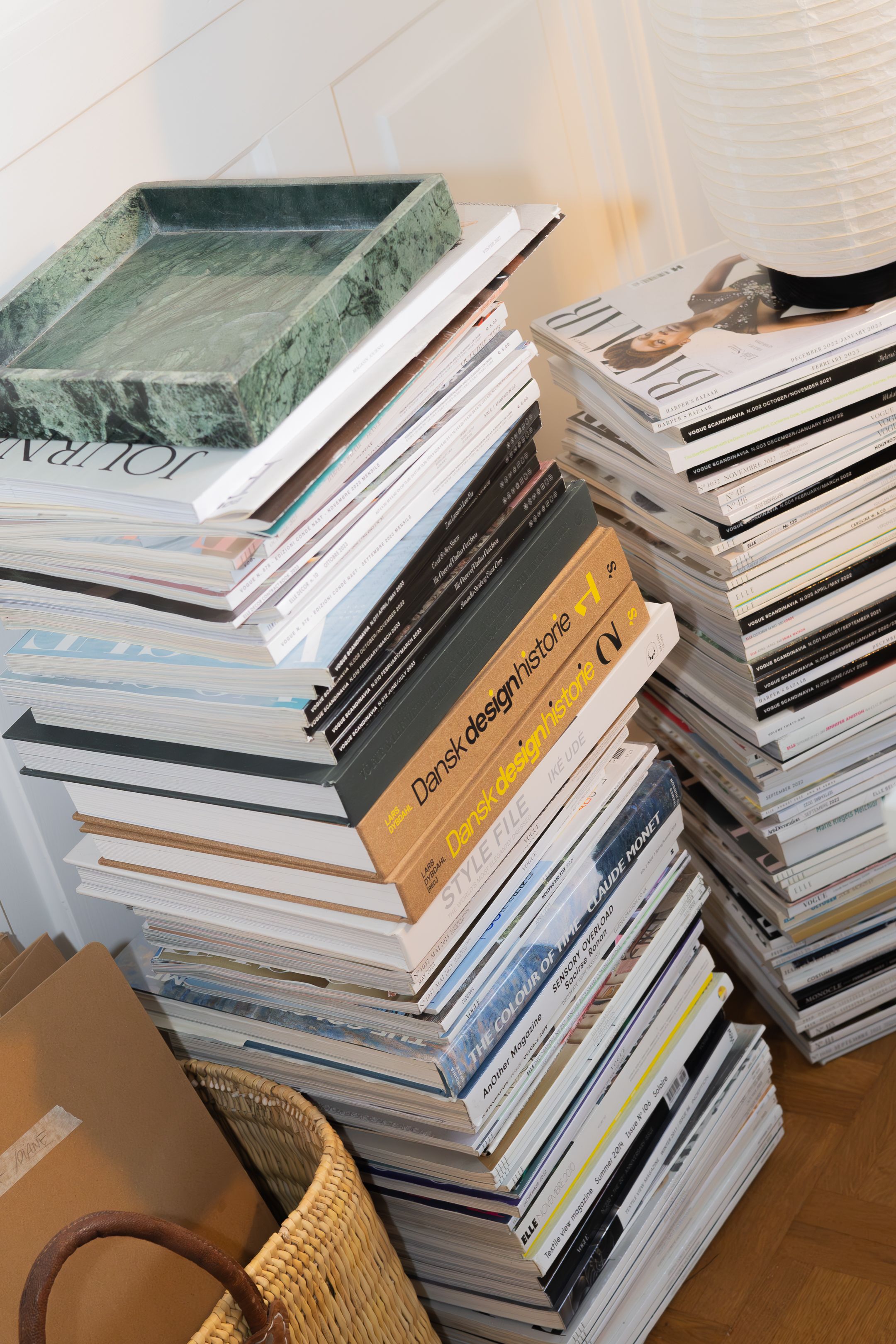 Stack of magazines and books with decorative green tray on wooden floor.