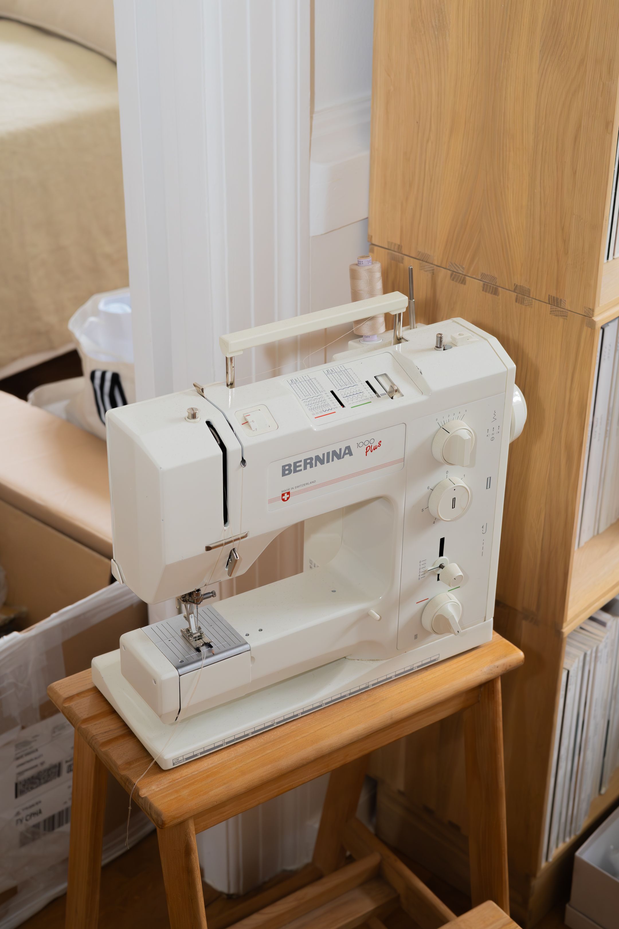 White Bernina sewing machine positioned on wooden stool next to storage unit.