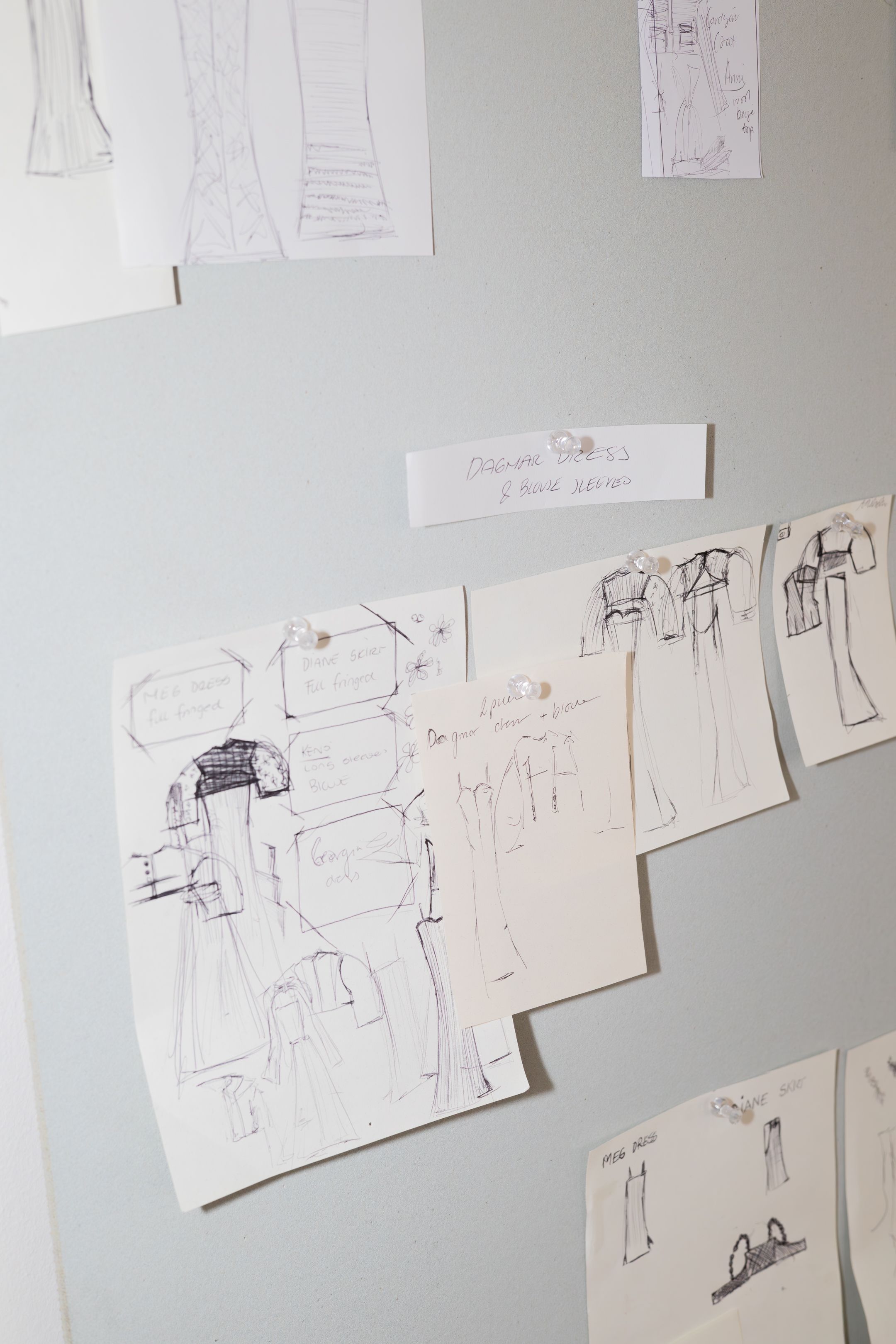 Fashion design sketches and technical drawings displayed on grey wall.