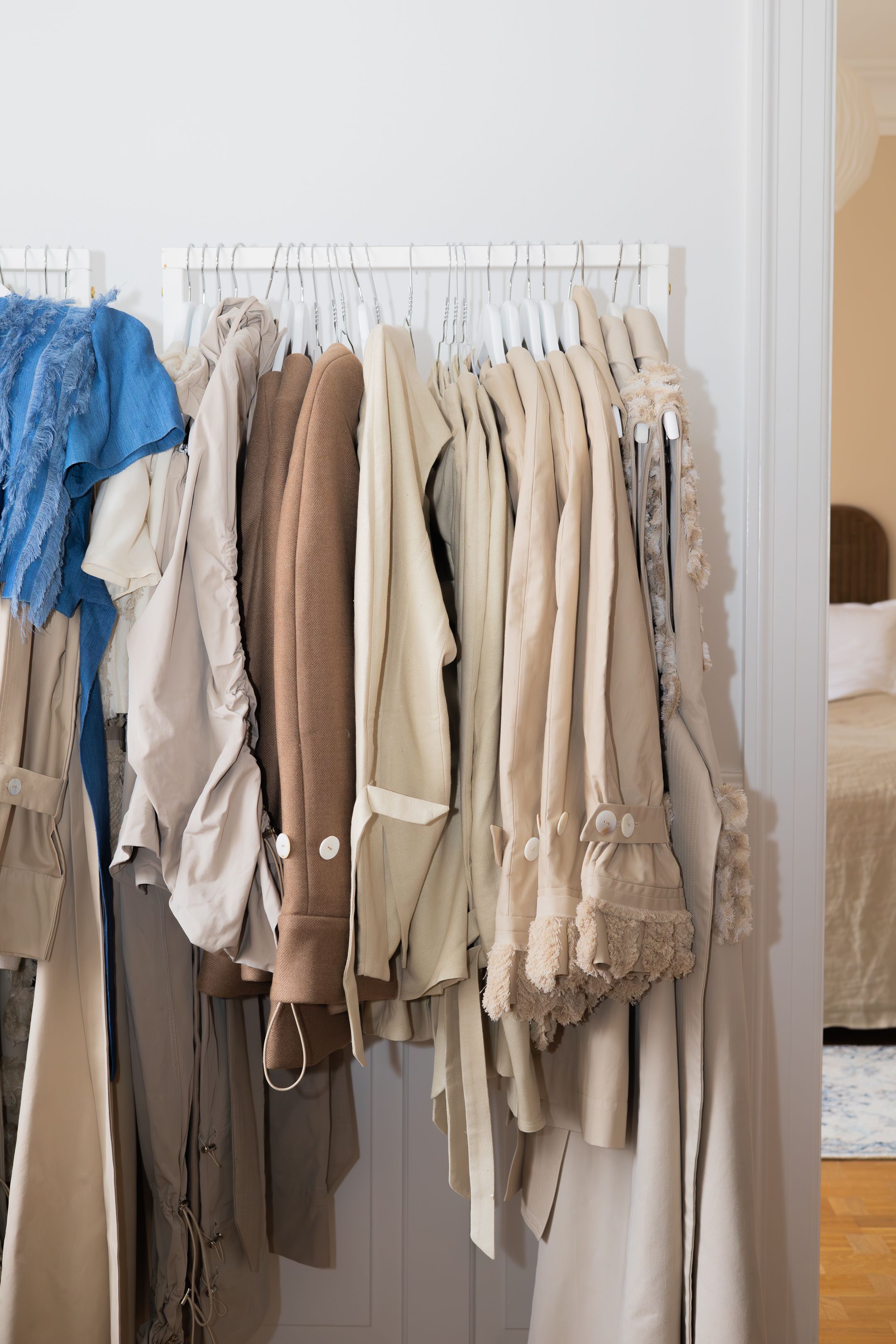 Rack of neutral-colored clothing hanging on white hangers.