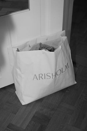 White shopping bag with Arisholm branding on wooden floor.