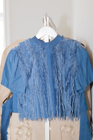 Blue denim top with distressed lace detailing on a hanger.