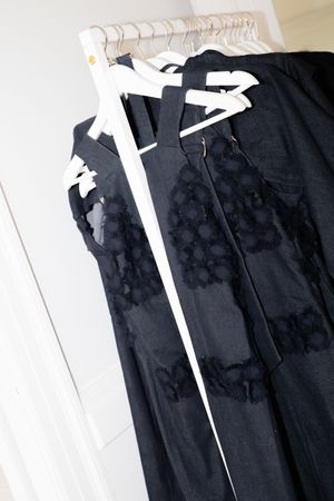 Black formal dress with lace details and white trim hanging in closet.