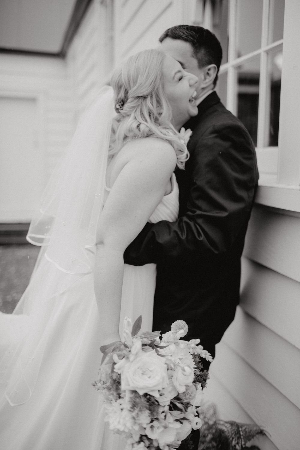 Black and white photo of romantic moment between newlyweds with bridal bouquet.