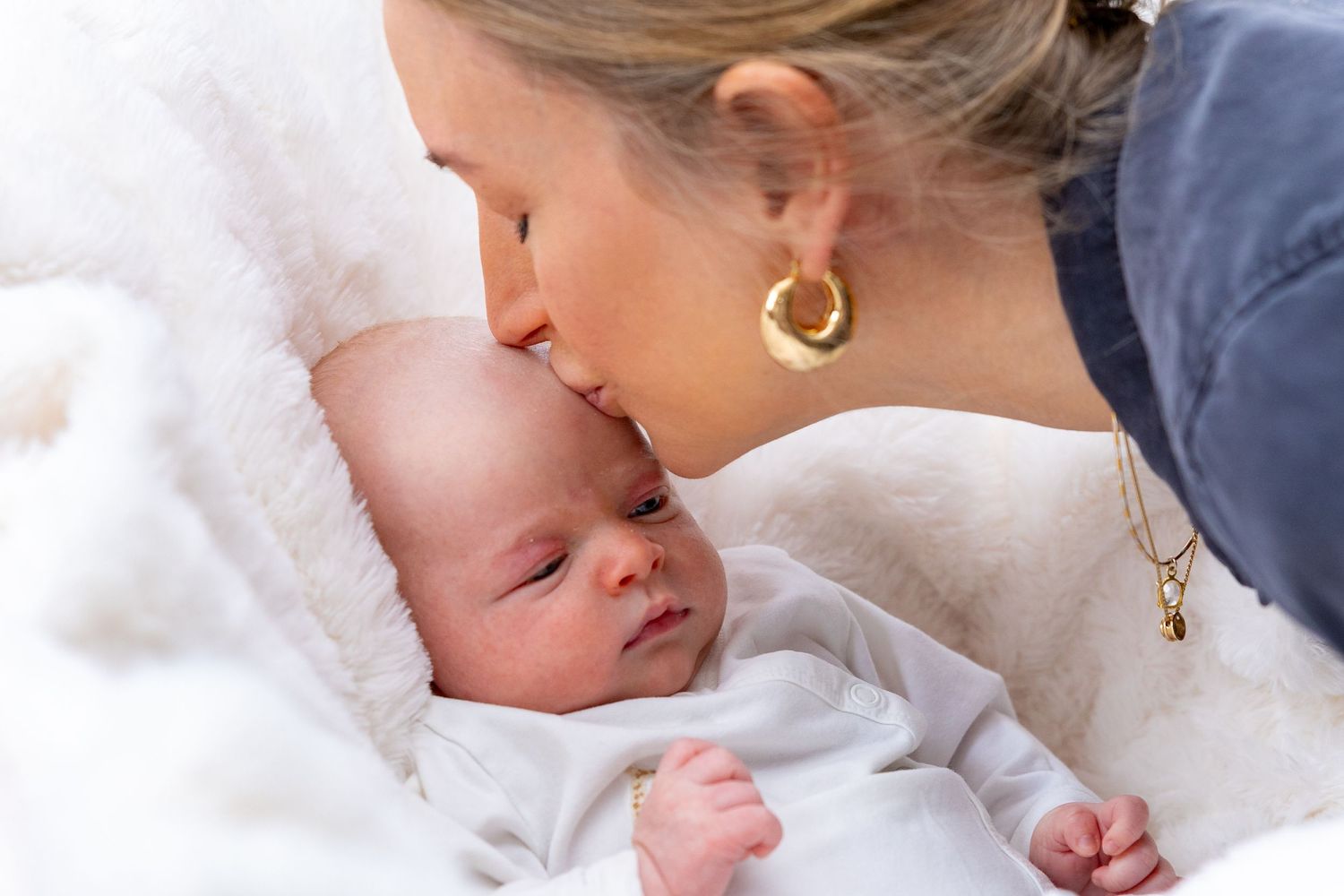 Tender moment between mother and newborn baby against white backdrop.