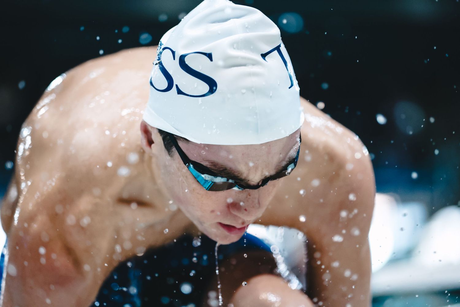 Competitive swimmer in white cap and goggles during winter training session with snow effects.