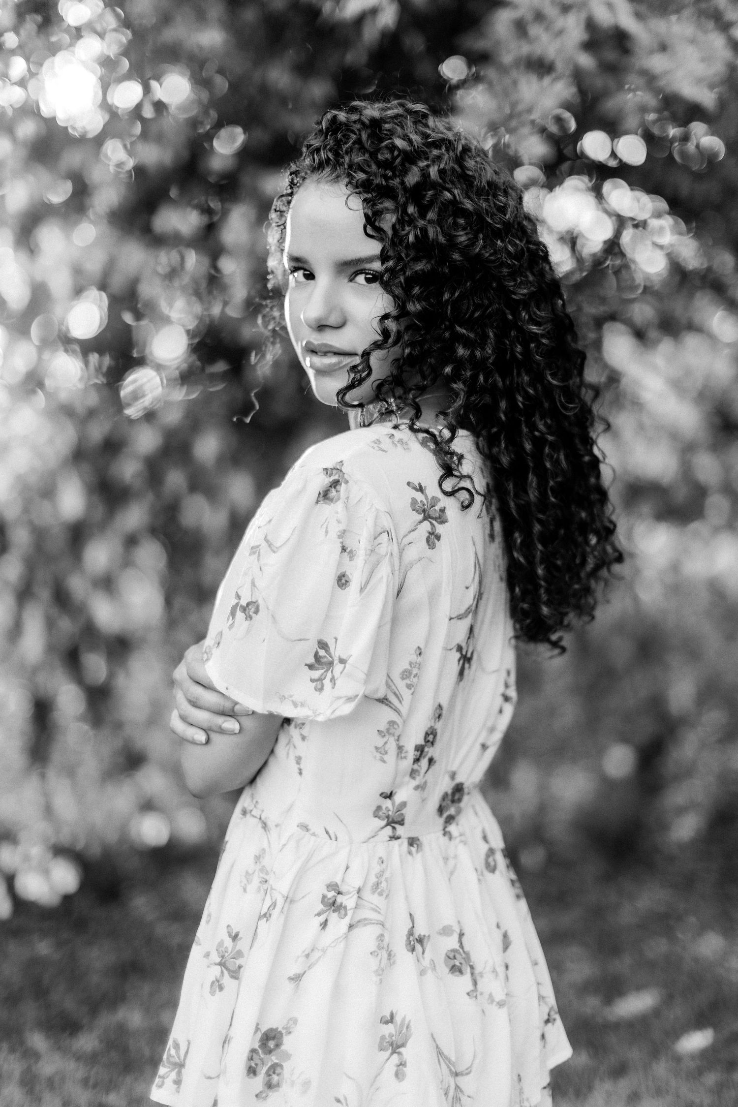 Black and white portrait of person in floral dress with natural curly hair outdoors.