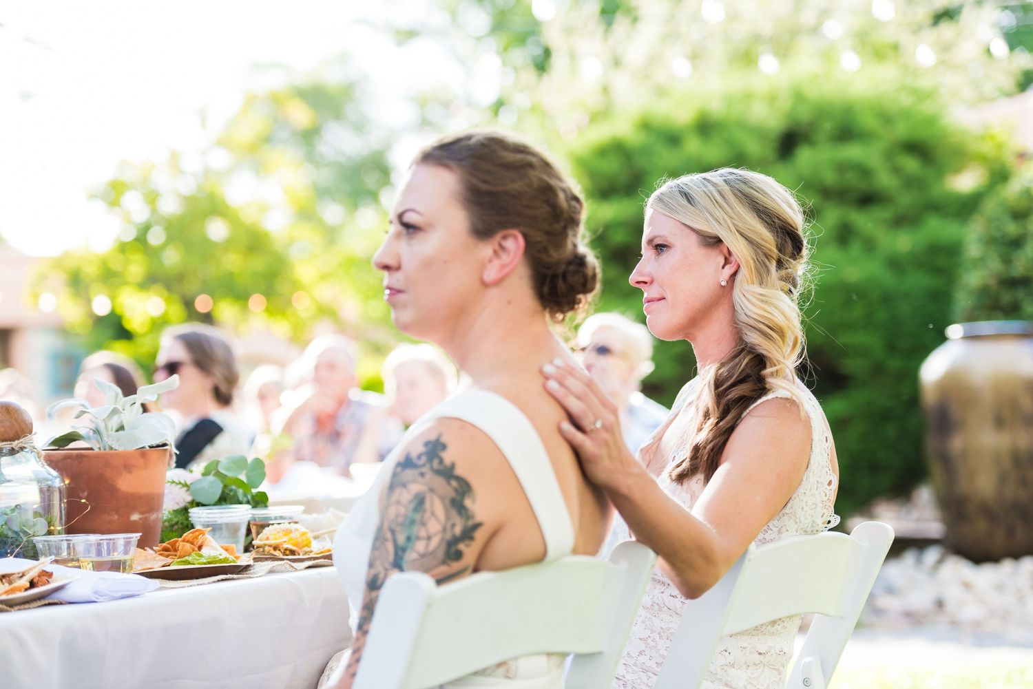 Outdoor wedding reception with guests dining at tables in a garden setting.