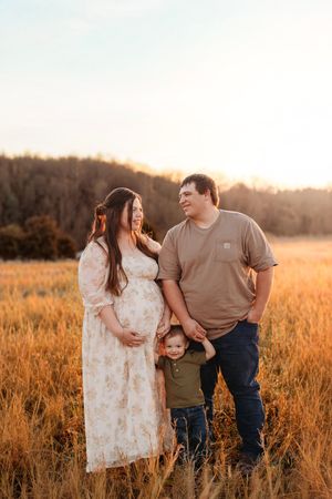 Family maternity portrait with pregnant mother, father, and toddler son in golden sunset field.