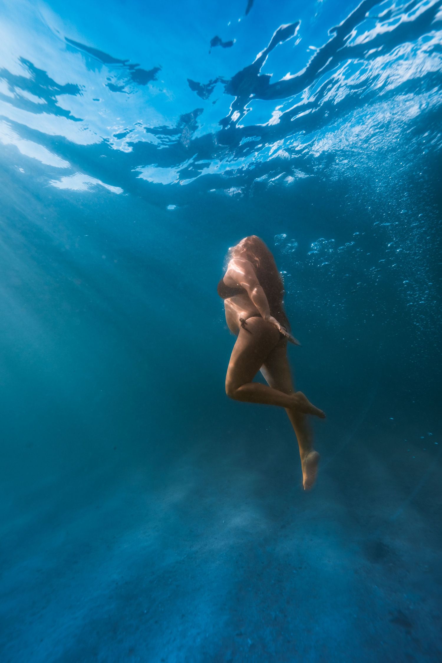 Underwater view of a person swimming in clear blue ocean water with sunlight rays filtering through the surface.