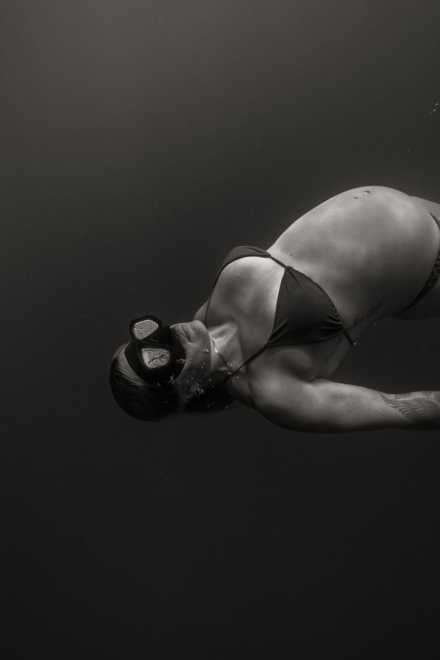 Black and white artistic photo of a person lying on a dark background wearing a swimsuit and goggles.
