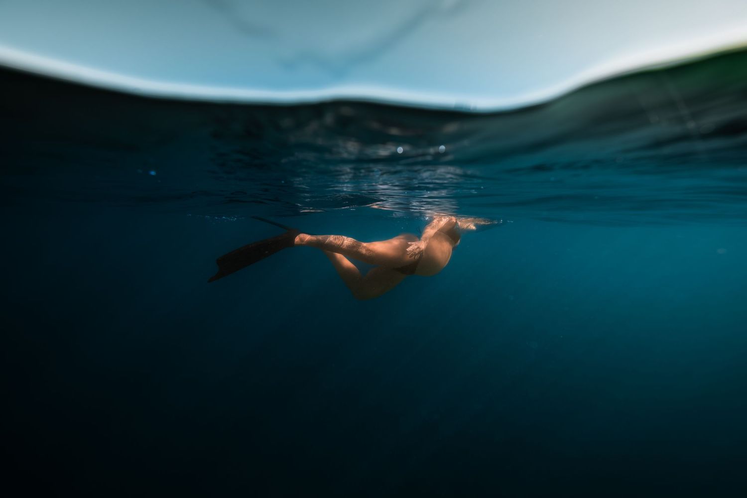 Underwater split view photography showing a person floating in tranquil blue ocean waters at sunset.
