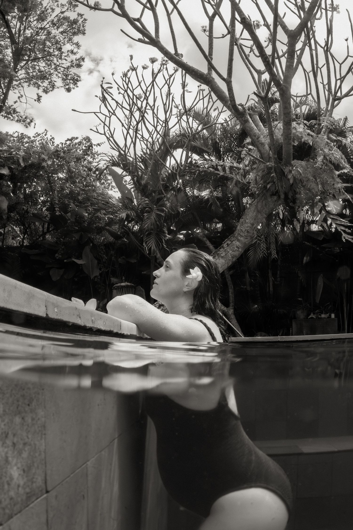 Swimming underwater in a backyard pool shows a person diving backwards in black and white photography.