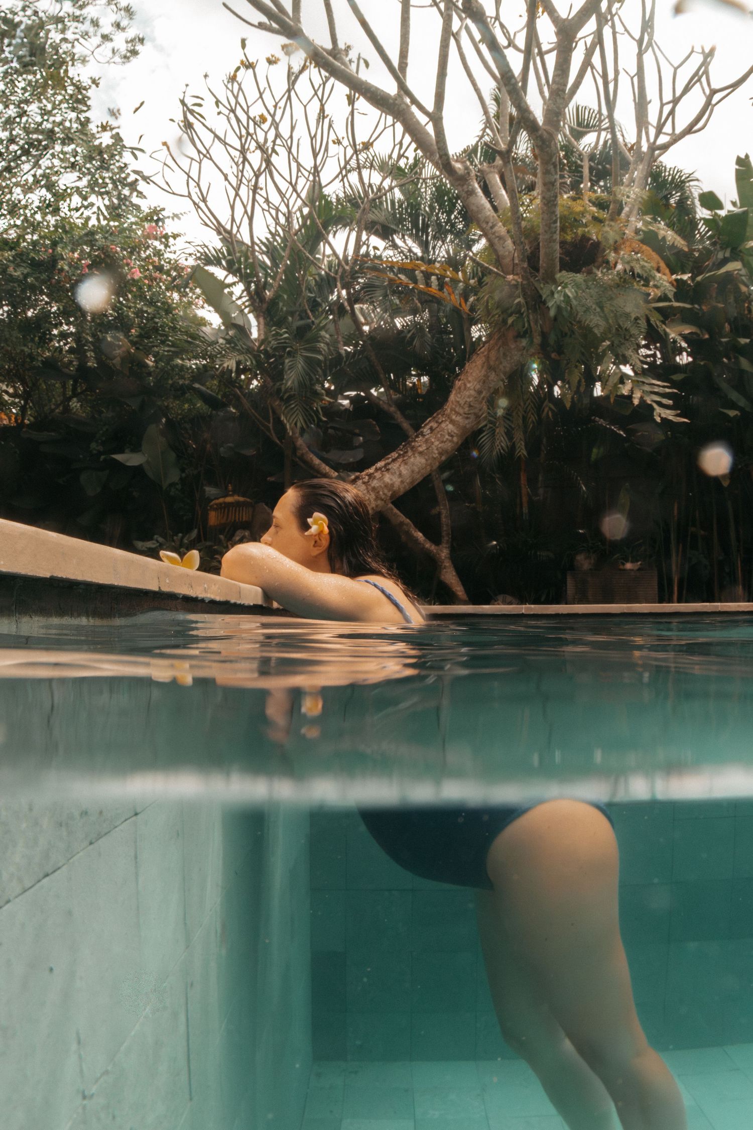 Split view of a peaceful swimming pool surrounded by tropical trees with someone relaxing on a pool float.