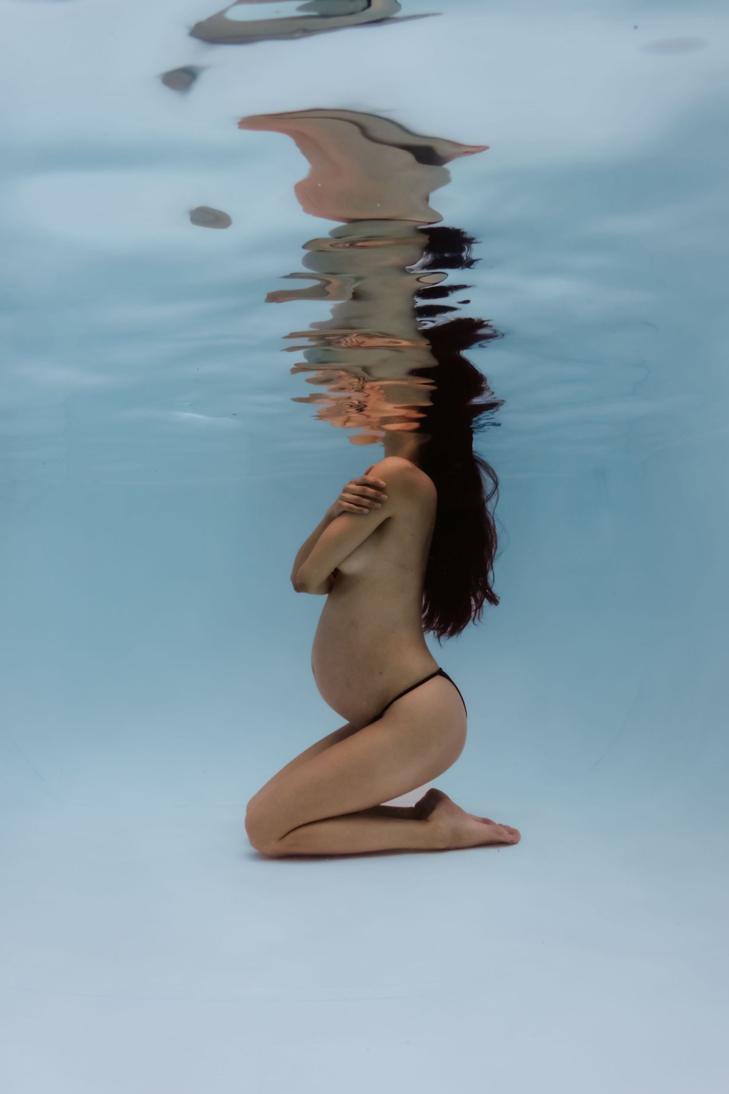 Pregnant woman kneeling underwater in a pool, captured in a serene maternity photography session.