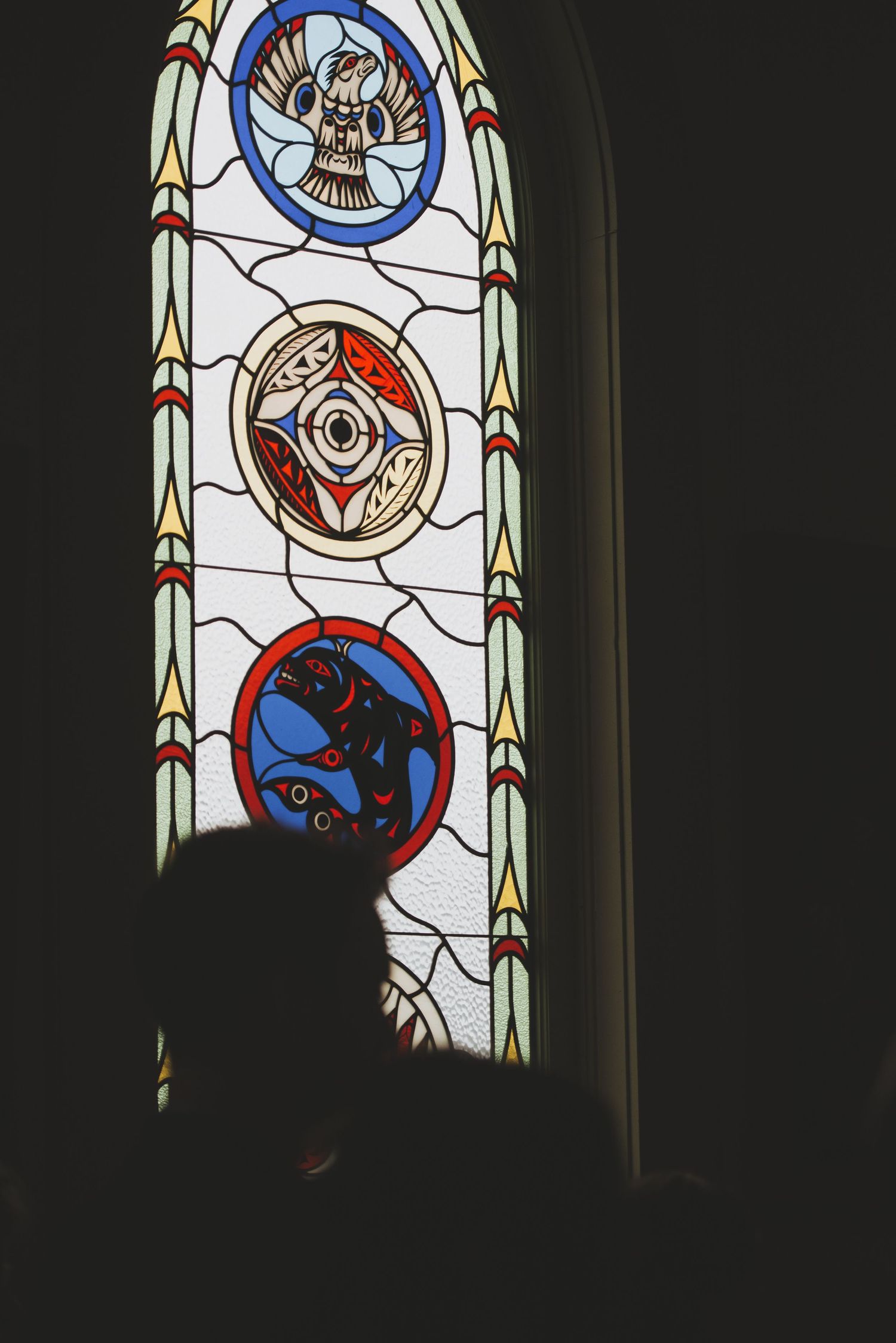Decorative stained glass church window featuring three circular medallions with religious symbols and motifs.