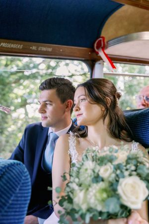 A couple sits side by side in a vintage car on their wedding day, holding a white floral bouquet. Essex Wedding Photographer