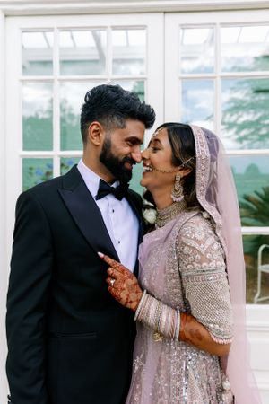 A couple shares an intimate moment by a window wearing traditional South Asian wedding attire. Essex Wedding Photographer