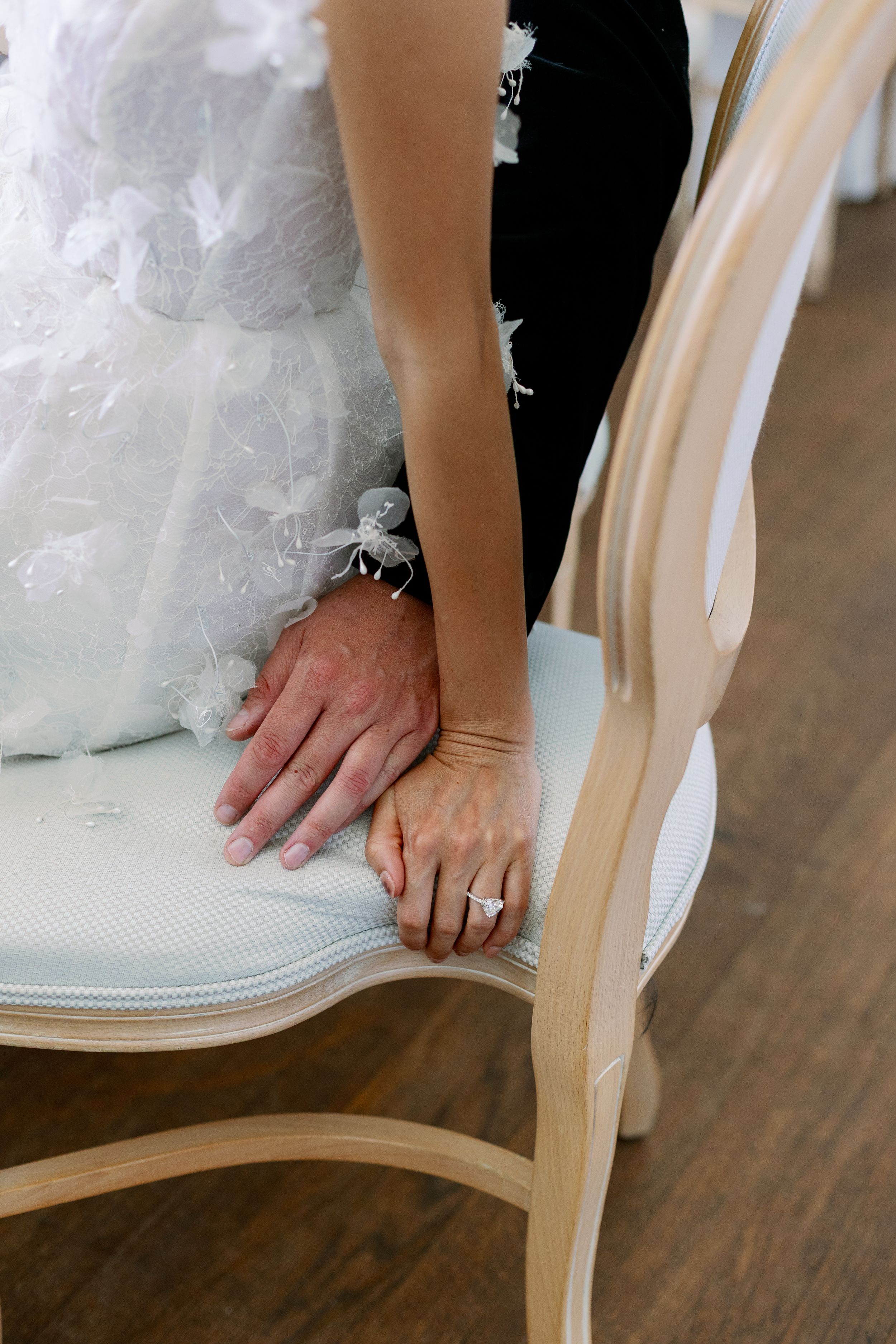 A close-up view of hands resting on a white upholstered chair with tulle from a wedding dress visible.