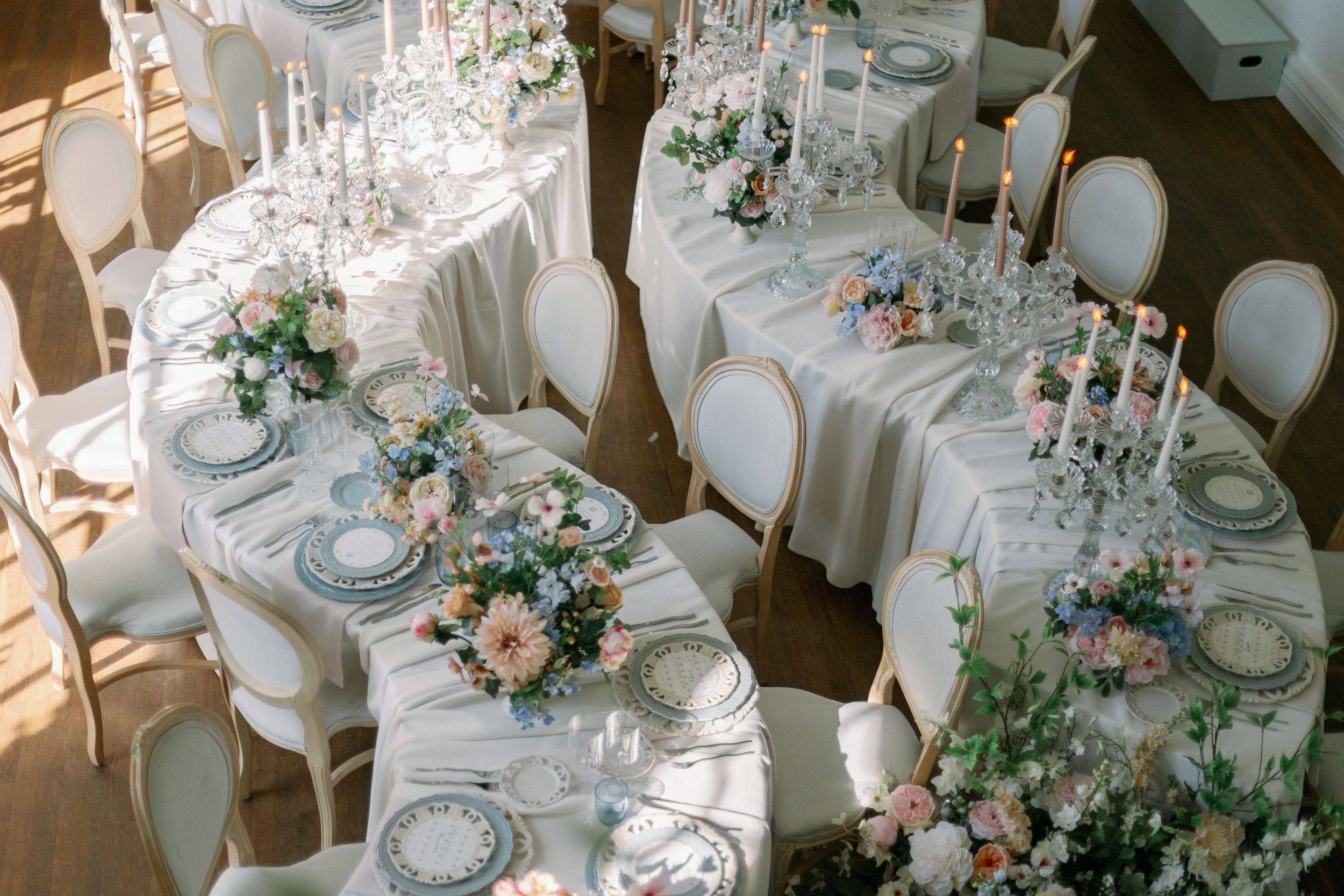 Elegant wedding reception tables with white linens, crystal candelabras, pink floral centerpieces and formal place settings.