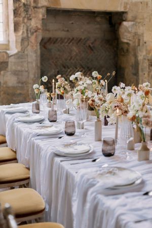 Elegant table setting with white linens and neutral floral centerpieces in a rustic stone venue. Essex Wedding Photographer