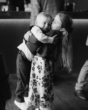 A heartwarming black and white image shows two children embracing, with a girl in a floral dress holding a small child.