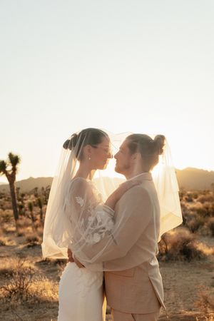 A romantic desert wedding photo at sunset with Joshua trees in the background and a flowing white veil.