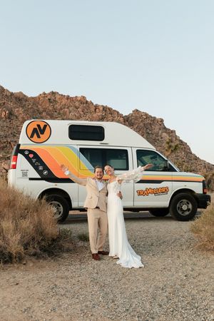 A decorated white van parked in a desert landscape with rocky mountains in the background during a photo session.