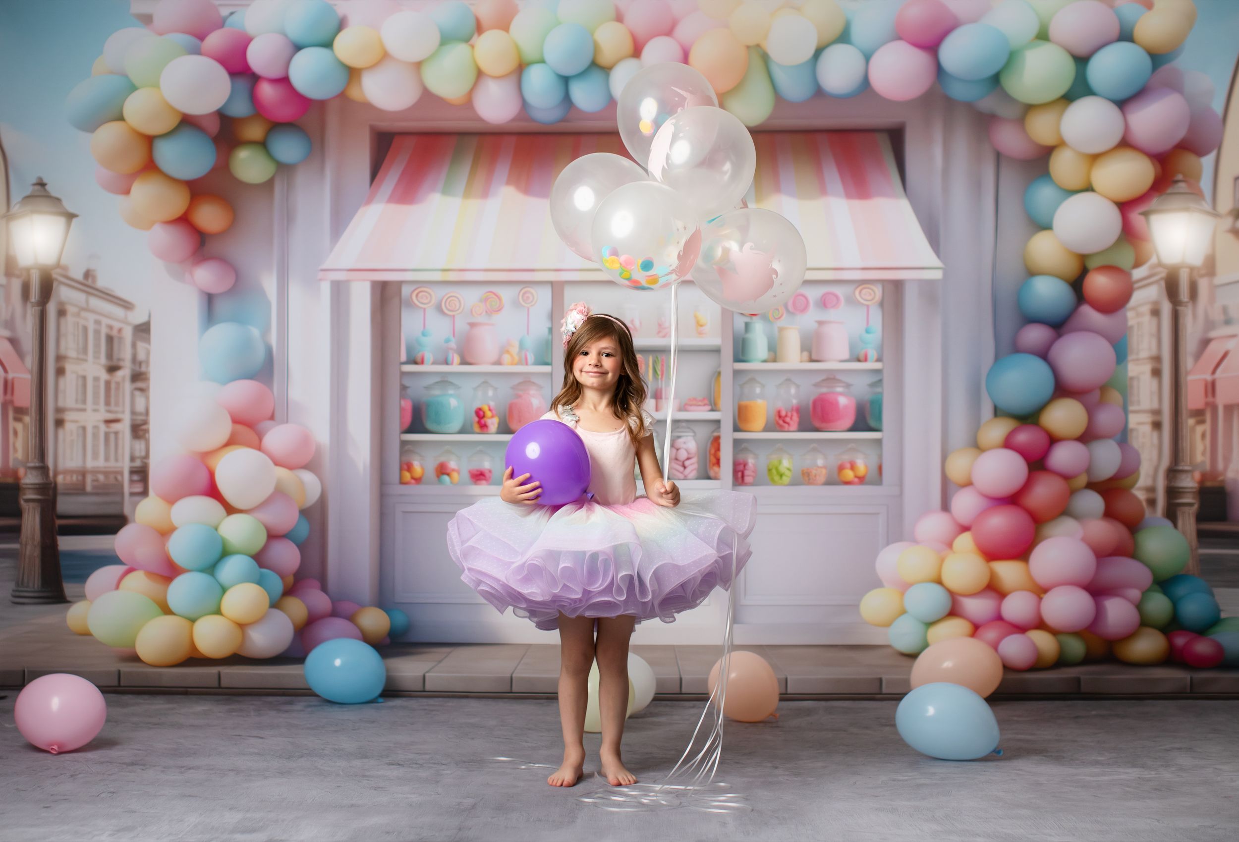 Whimsical ballet dancer portrait in purple tutu against pastel balloon arch and candy shop backdrop.