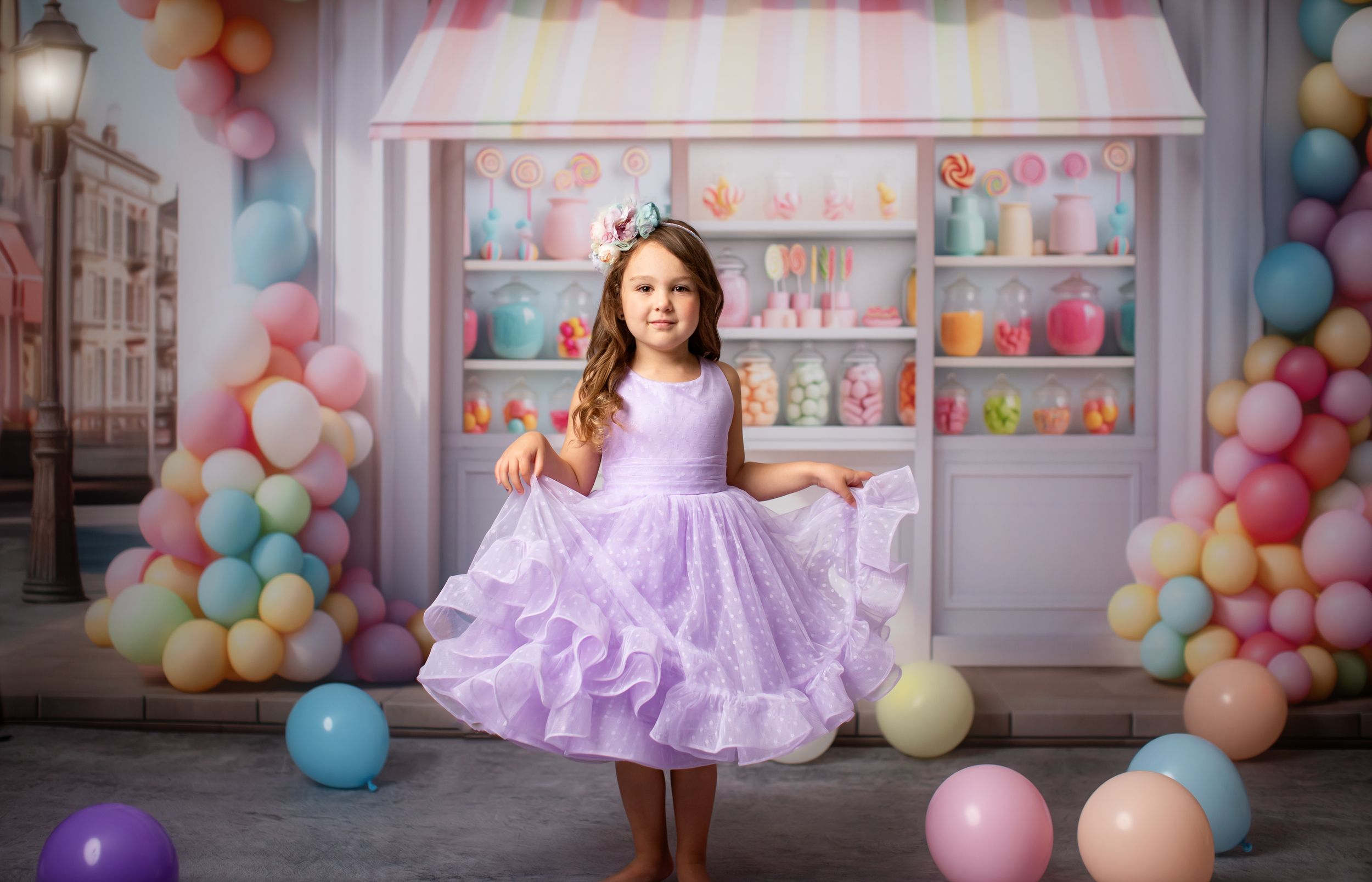 Portrait of dancer in purple ruffled dress against pastel balloon arch and candy shop backdrop.
