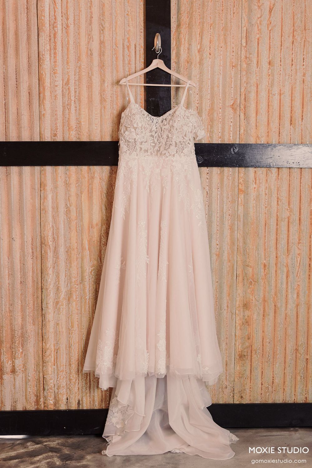 White wedding dress with delicate lace details hangs elegantly against a rustic wooden wall in a bridal studio.