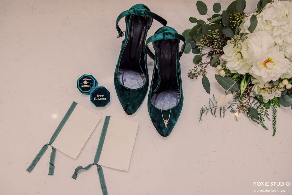 Elegant teal wedding shoes and accessories arranged with white floral bouquets and paper elements on a light surface.