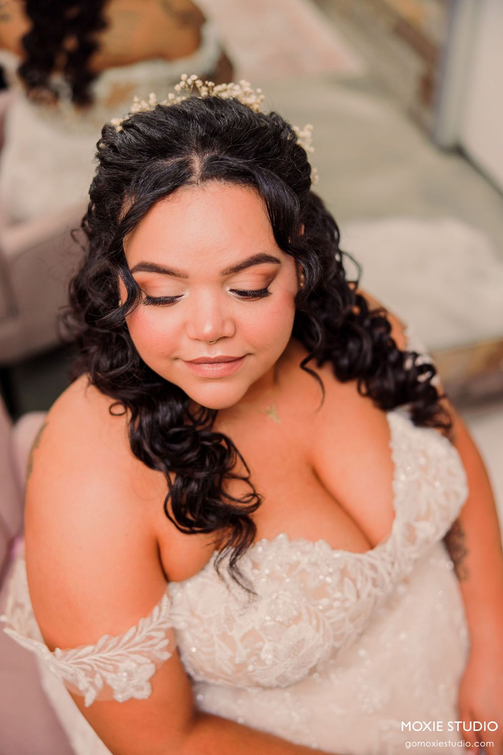 A radiant bride wearing a delicate lace wedding dress and crystal headpiece with flowing dark curls and natural makeup.