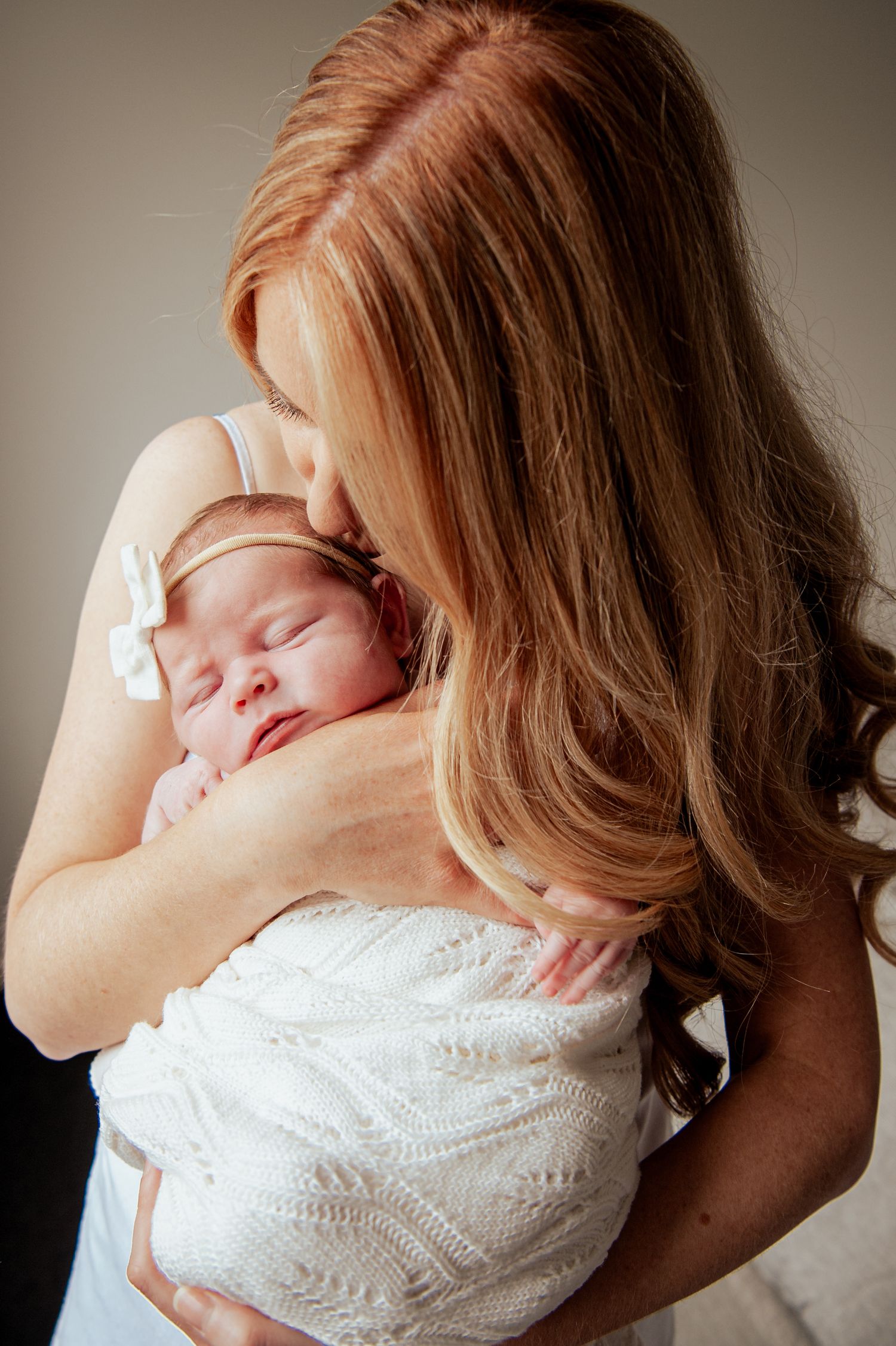 A sleeping newborn wrapped in white lace is held close against someone with long red hair.
Altona Family Photographer Melbourne