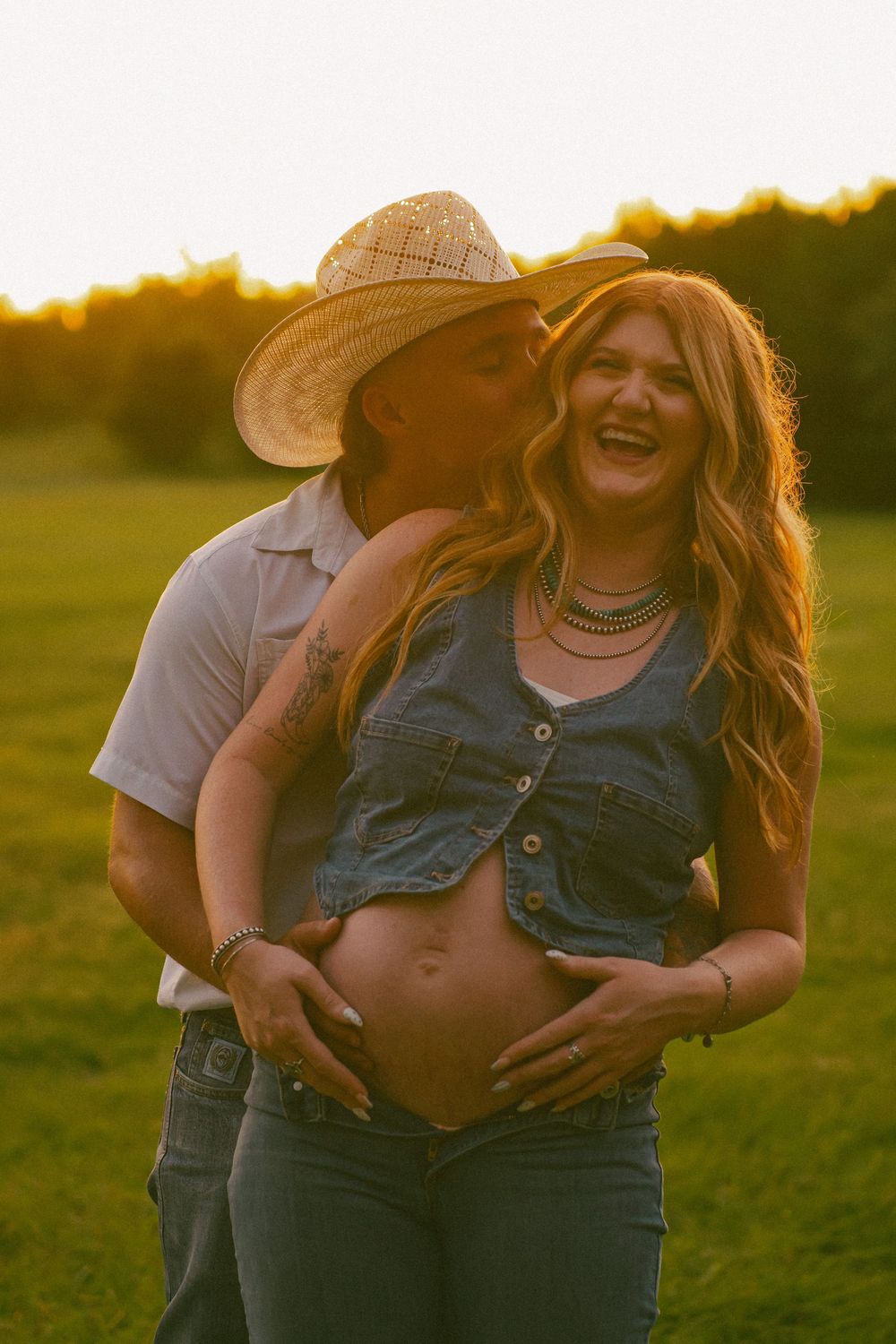 A couple shares a joyful moment in denim outfits during sunset in a field.