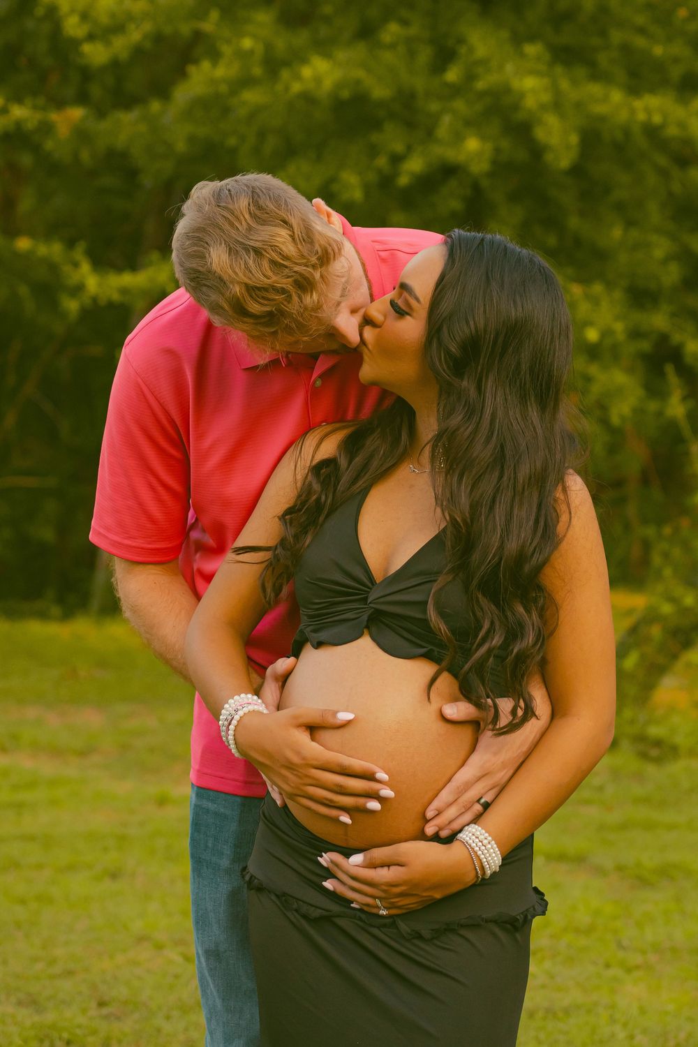 A romantic couple embraces tenderly in a grassy outdoor setting during golden hour.