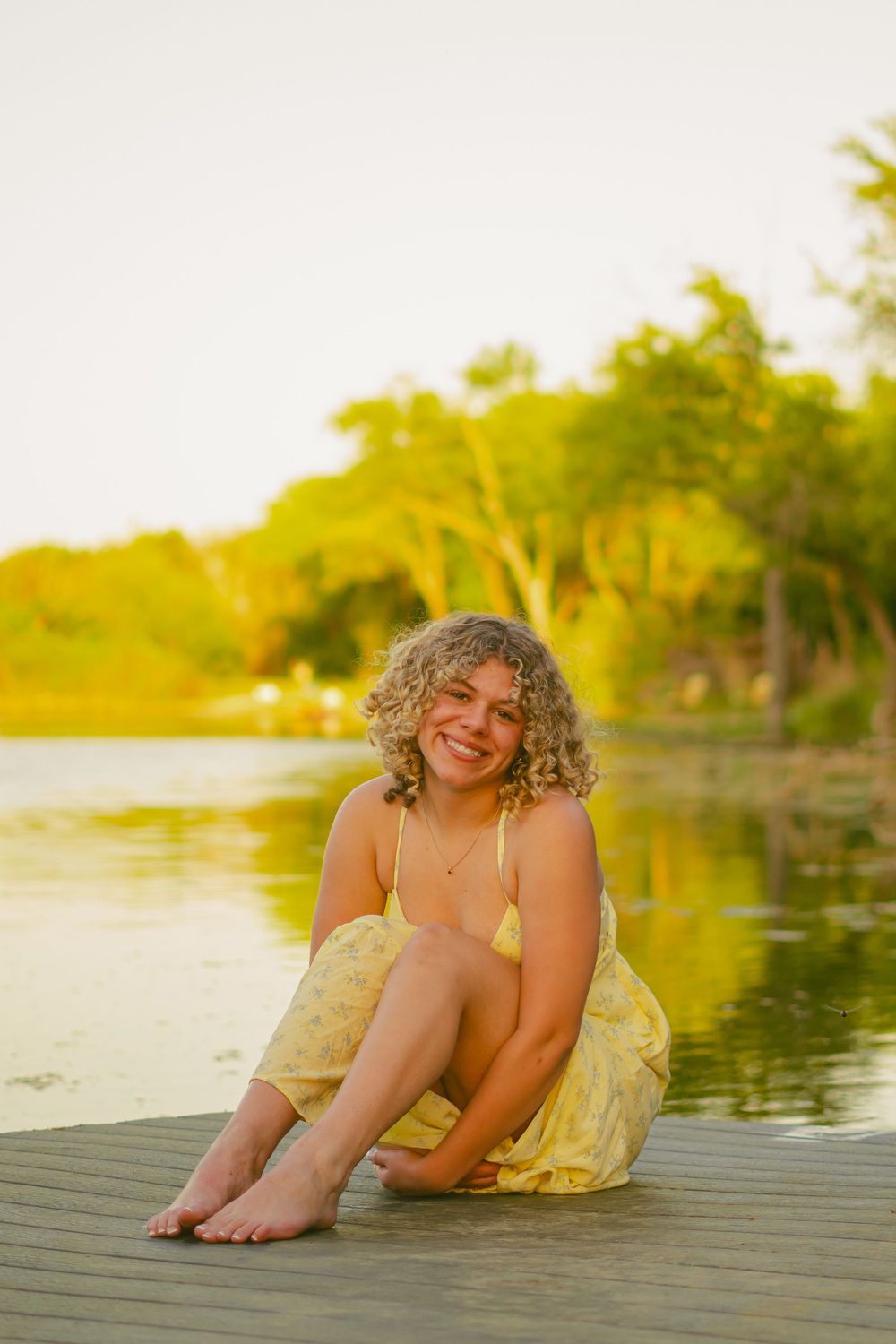 Person in yellow dress reclining on wooden dock during golden hour sunset.