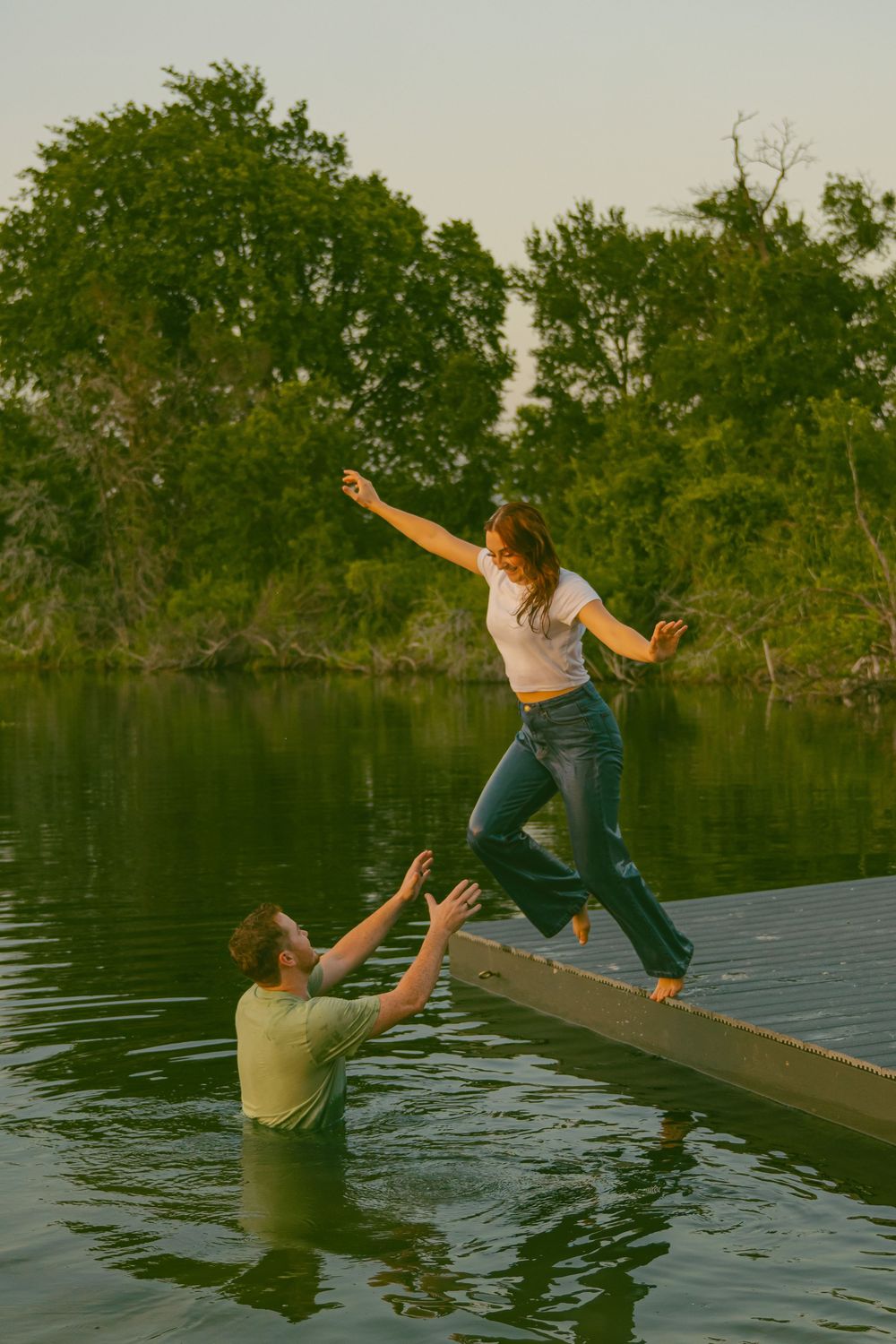 A playful scene of someone jumping into a lake from a wooden dock at sunset.