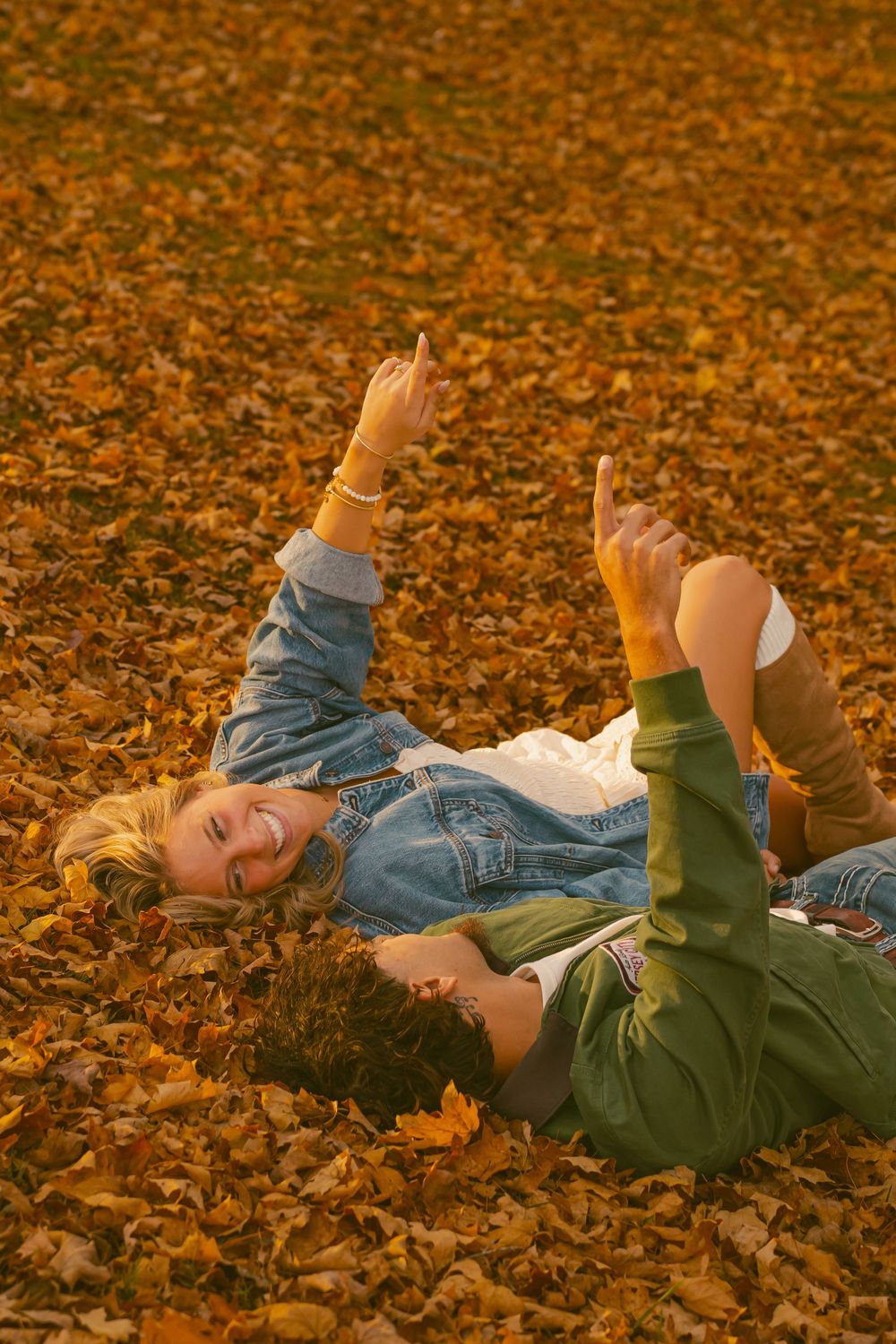 Person lying in fallen autumn leaves making playful gestures.