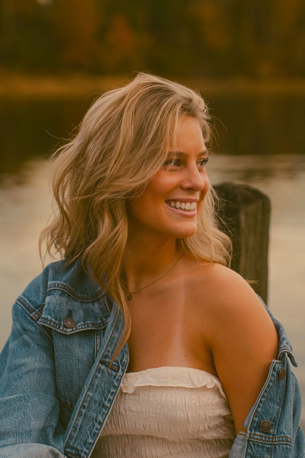 Portrait of someone wearing denim jacket by water during sunset.