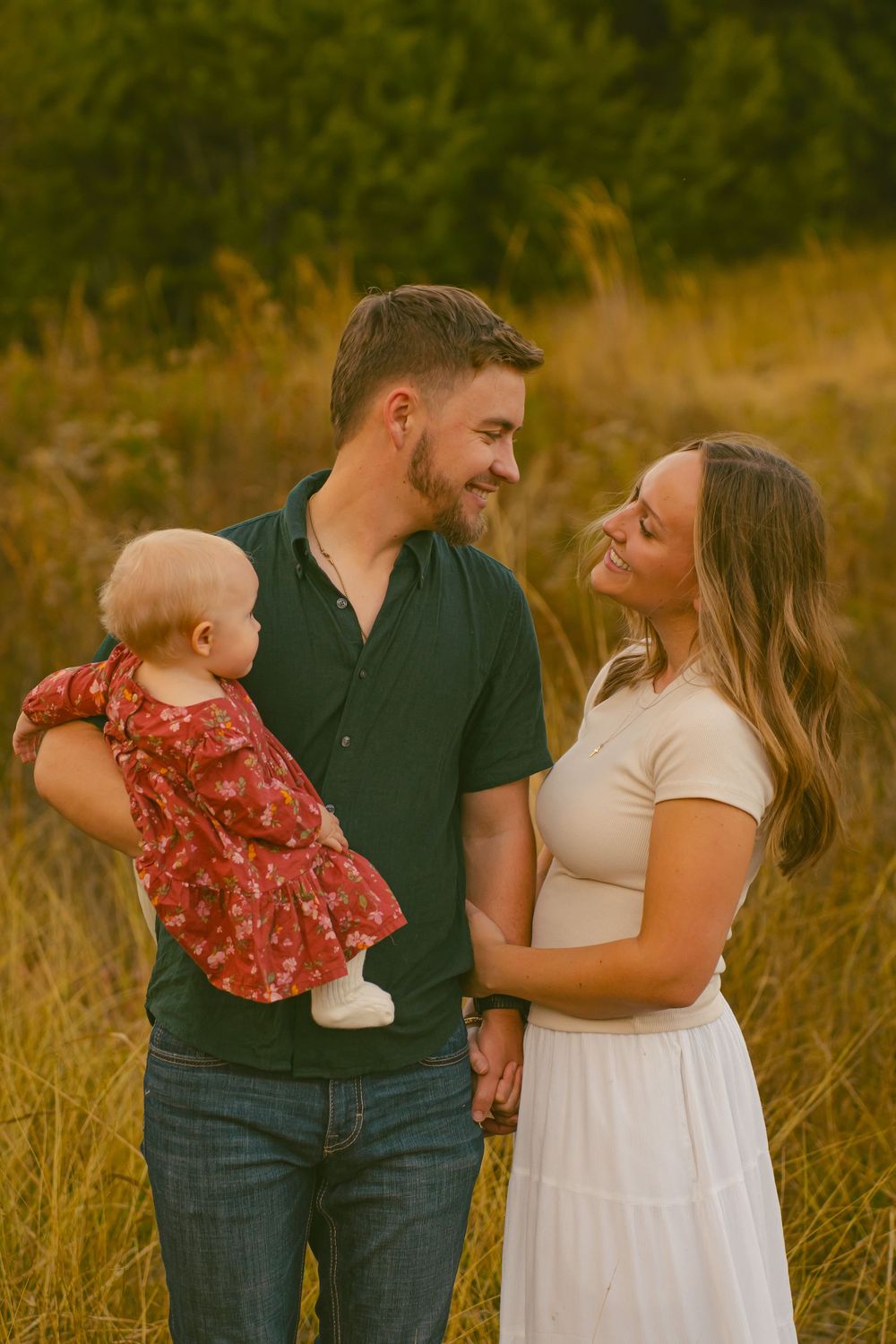 A happy family moment with parents and baby in a sunlit field.